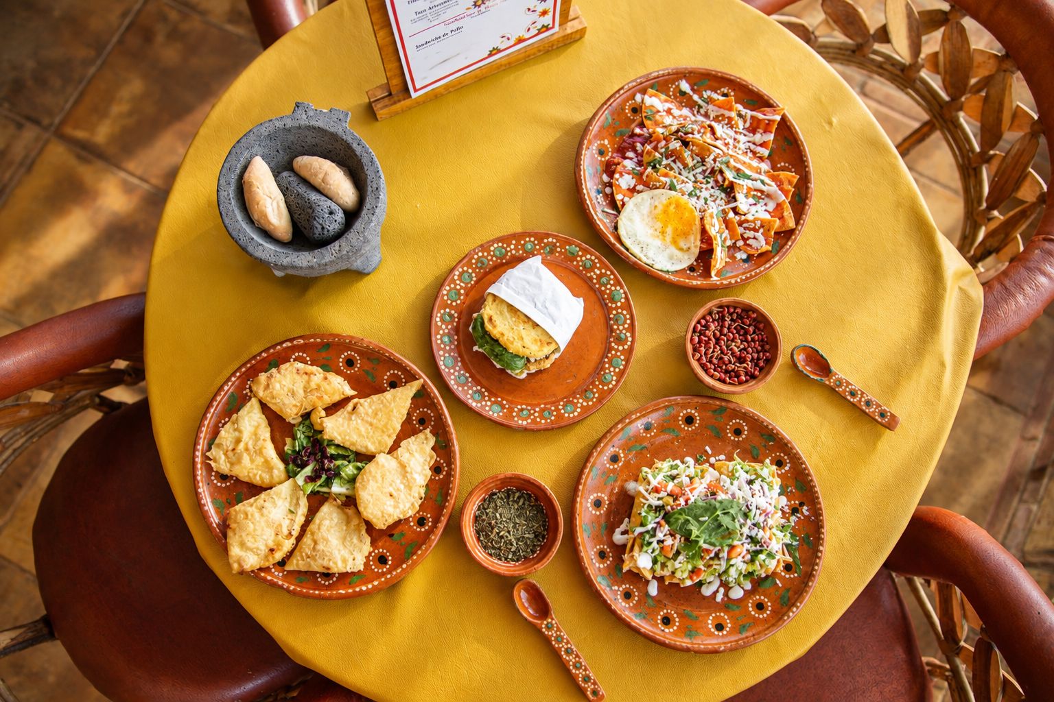 Vista de la mesa amarilla con chilaquiles, gordita, empanadas y molcajete