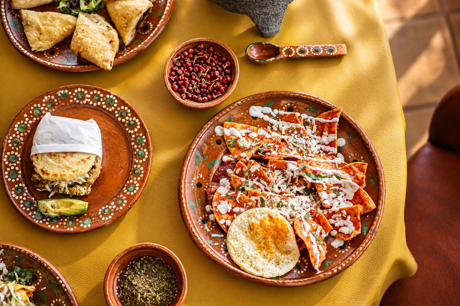 Chilaquiles rojos con huevo estrellado, gordita de chicharrón y empanadas sobre mantel amarillo