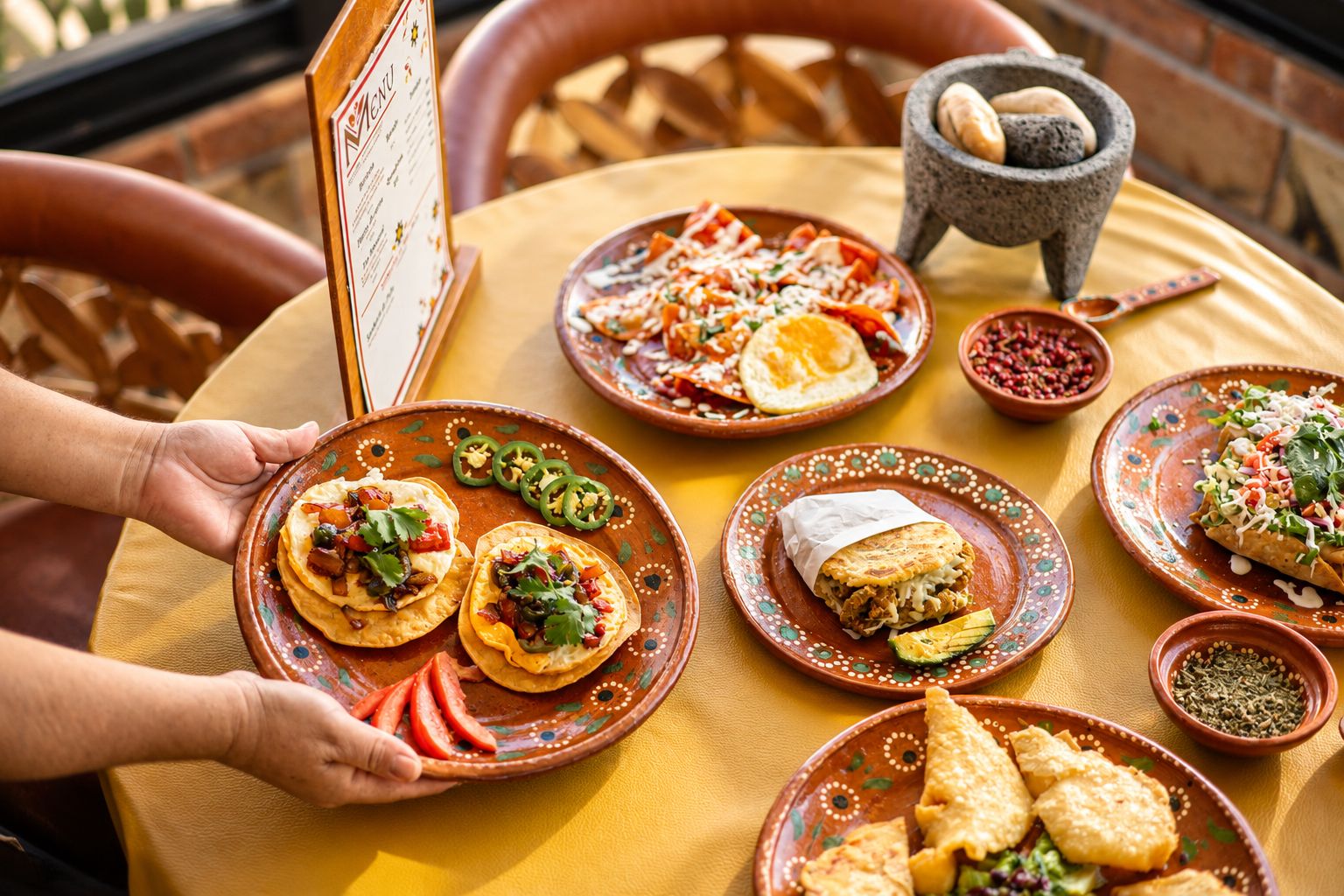 Mesa servida con sopes, chilaquiles y molcajete junto al menú