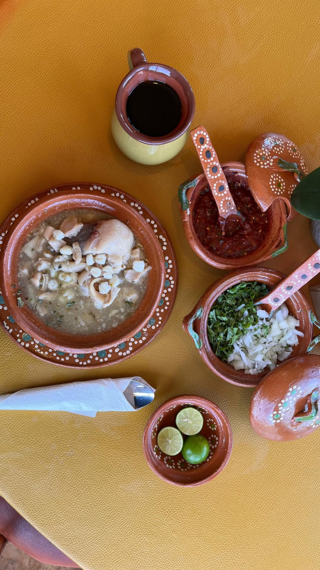 Mesa servida con pozole, salsa, cebolla con cilantro, limones y café de olla